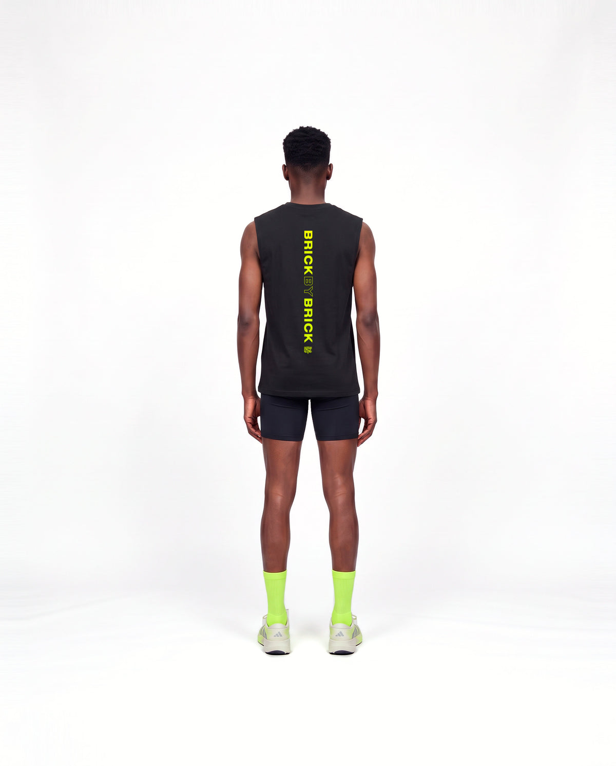 Model wearing the Brick by Brick tank top in black — back view with BRICK BY BRICK set vertically down the centre in lime green — View 4
