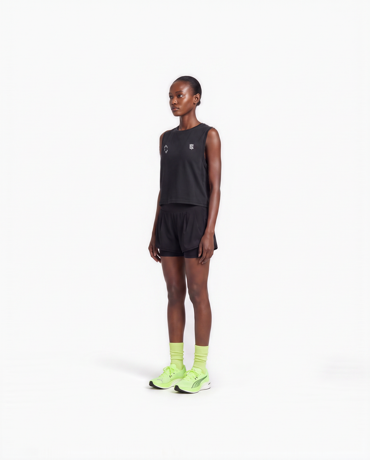 Model wearing the Let's Run the Night cropped tank top in black — three-quarter view showing the cropped fit — View 4