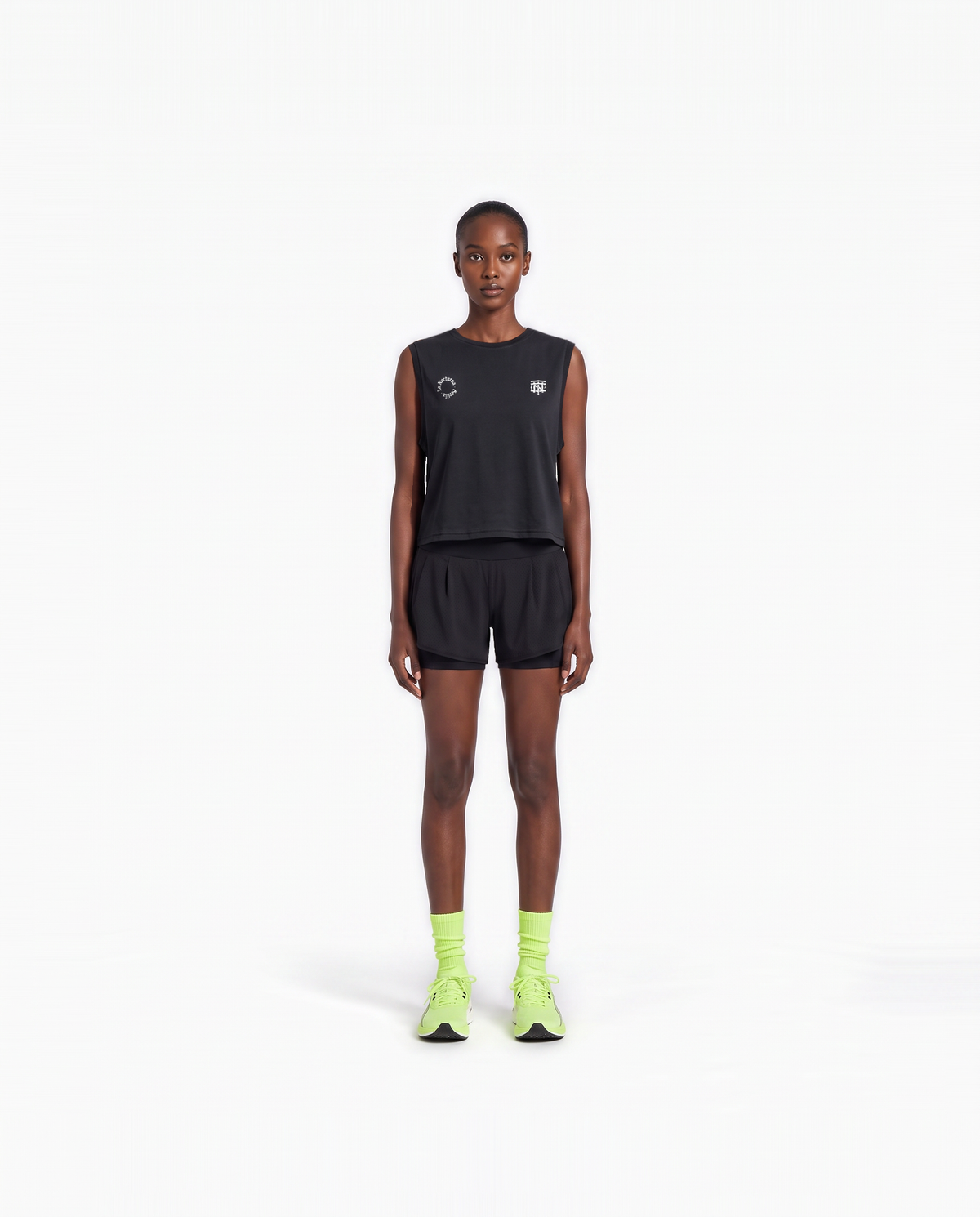 Model wearing the Let's Run the Night cropped tank top in black — front view with the La Nocturna Sevilla seal and the TN monogram in white — View 2
