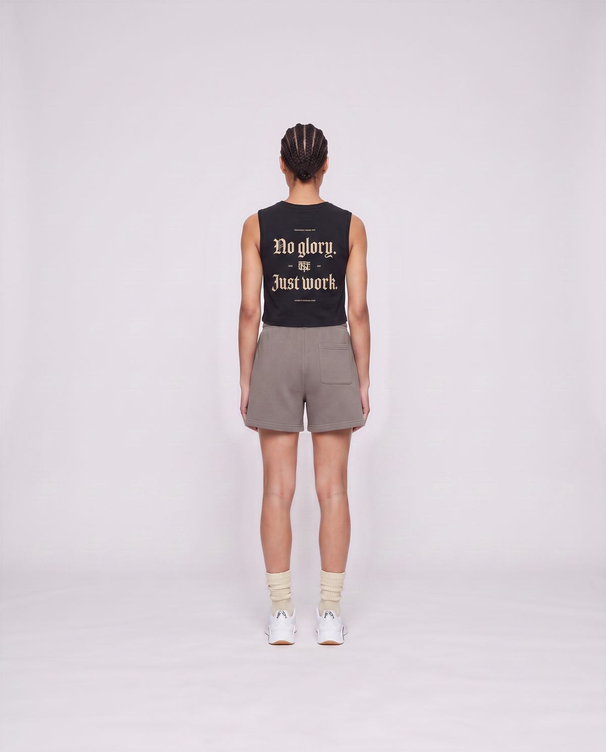 Model wearing the No Glory Just Work cropped tank top in black — back view with the NO GLORY JUST WORK blackletter print in sand with the Thundernoise monogram — View 4