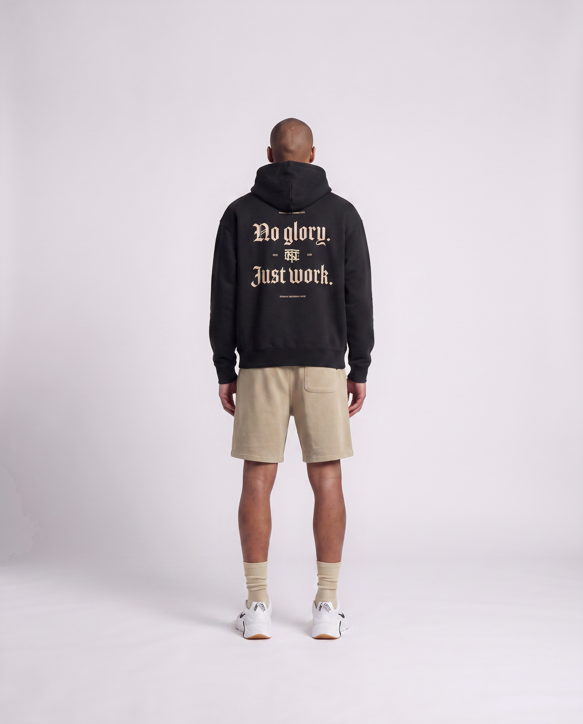 Model wearing the No Glory Just Work oversize hoodie in black — back view with the NO GLORY JUST WORK blackletter print in sand with the Thundernoise monogram — View 4