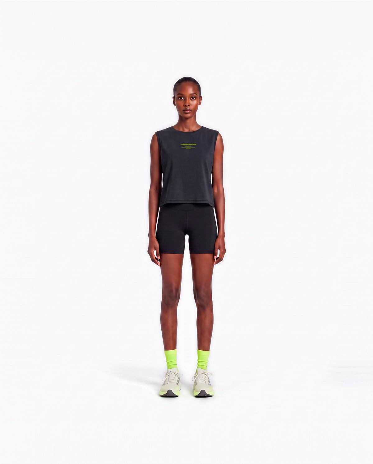 Model wearing the Brick by Brick cropped tank top in black — front view with the THUNDERNOISE TRAINING DEPT block centred on the chest in lime green — View 2
