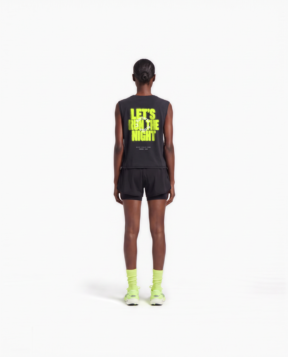 Model wearing the Let's Run the Night cropped tank top in black — back view with LET'S RUN THE NIGHT sprayed in electric lime around the La Nocturna Sevilla seal — View 6

