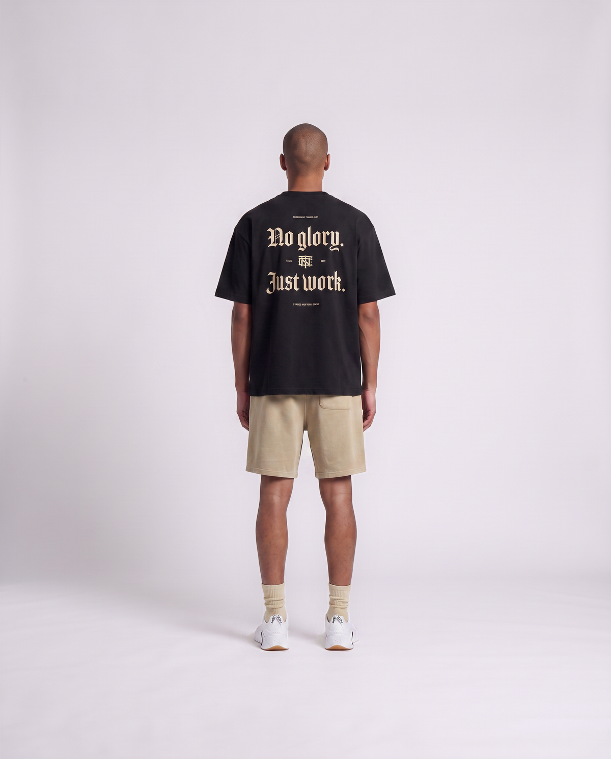 Model wearing the No Glory Just Work oversize t-shirt in black — back view with the NO GLORY JUST WORK blackletter print in sand with the Thundernoise monogram — View 4
