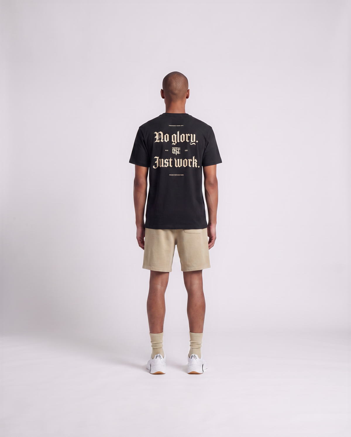 Model wearing the No Glory Just Work t-shirt in black — back view with the NO GLORY JUST WORK blackletter print in sand with the Thundernoise monogram — View 4
