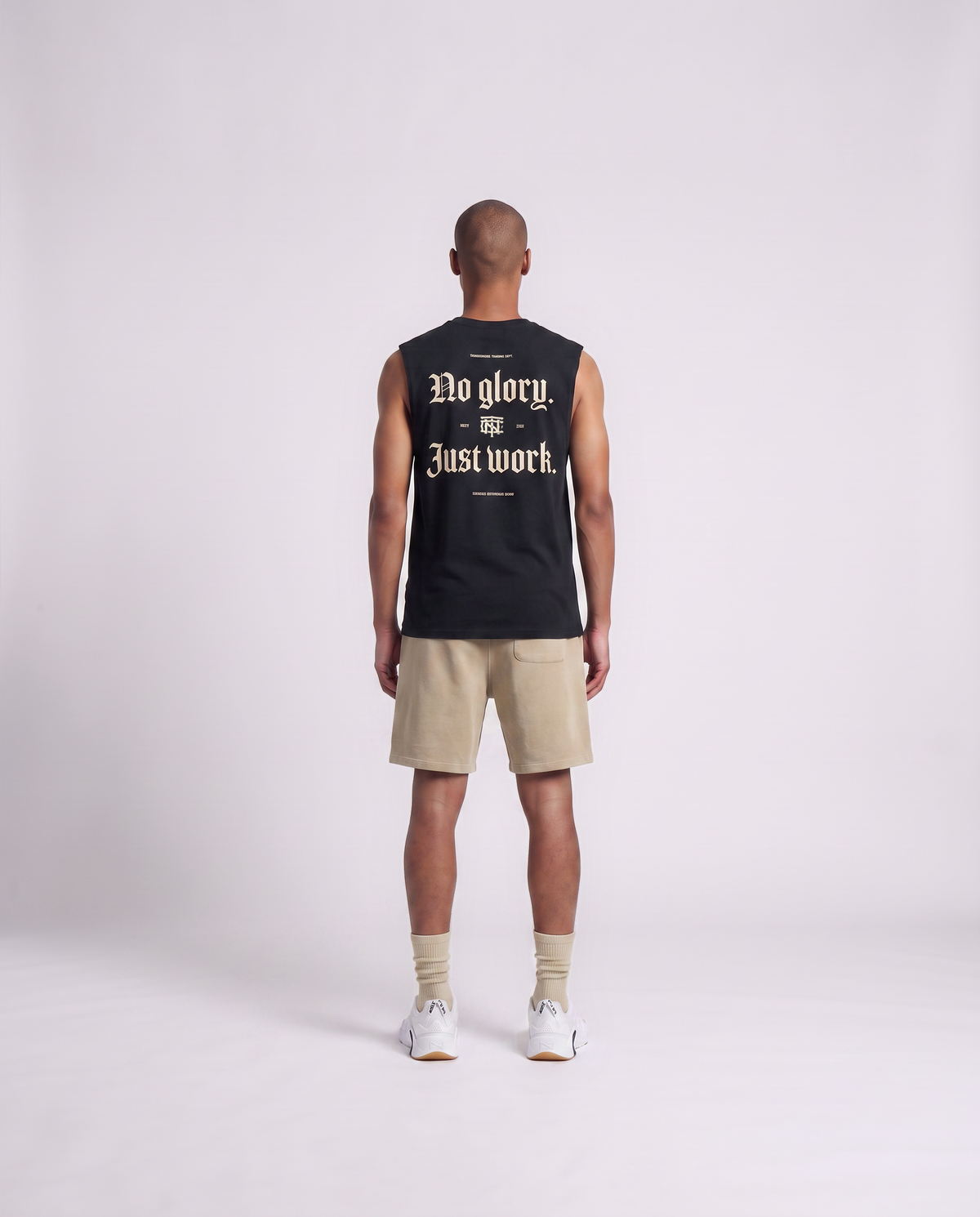 Model wearing the No Glory Just Work tank top in black — back view with the NO GLORY JUST WORK blackletter print in sand with the Thundernoise monogram — View 4
