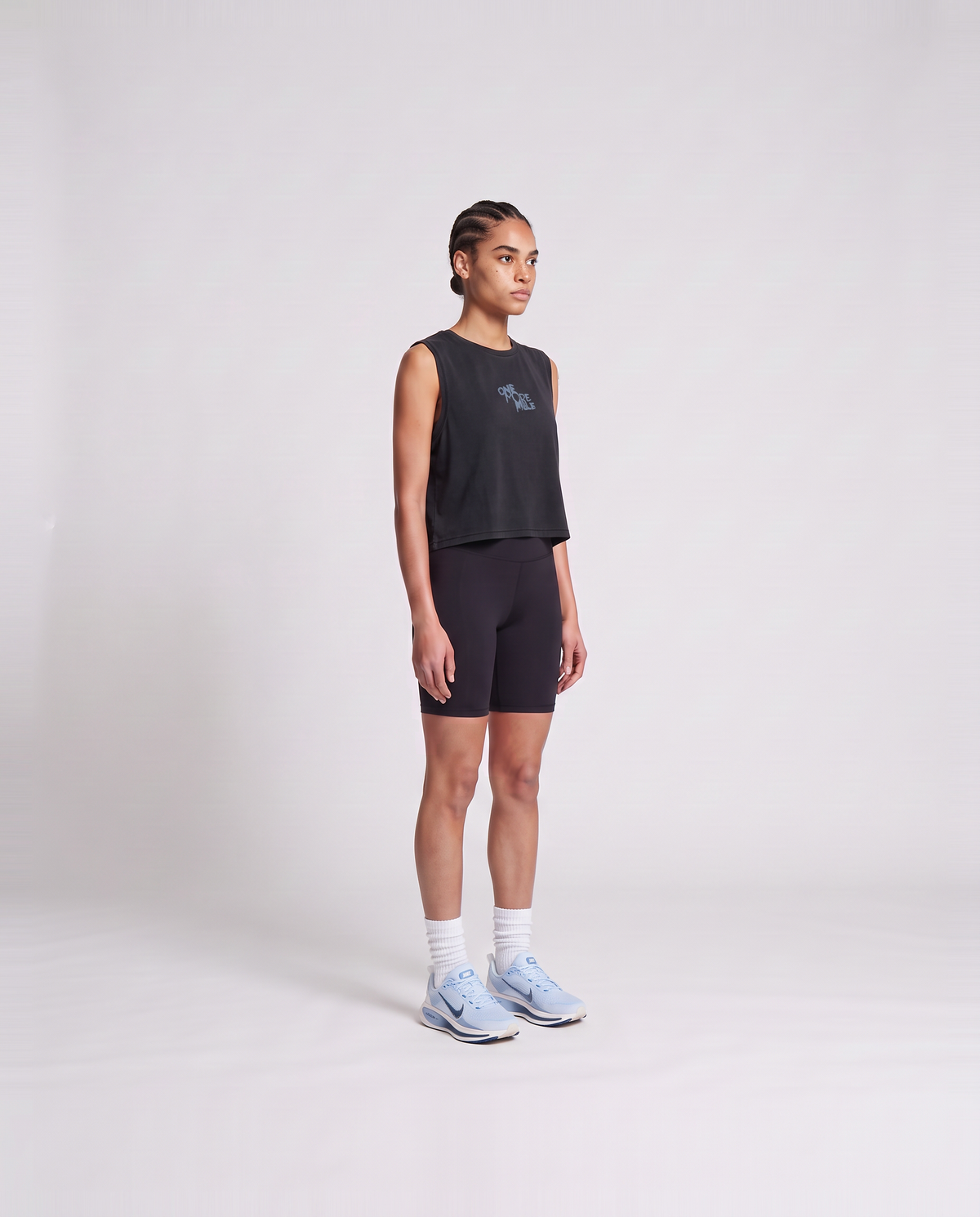 Model wearing the One More Mile cropped tank top in black — three-quarter view showing the cropped fit — View 3
