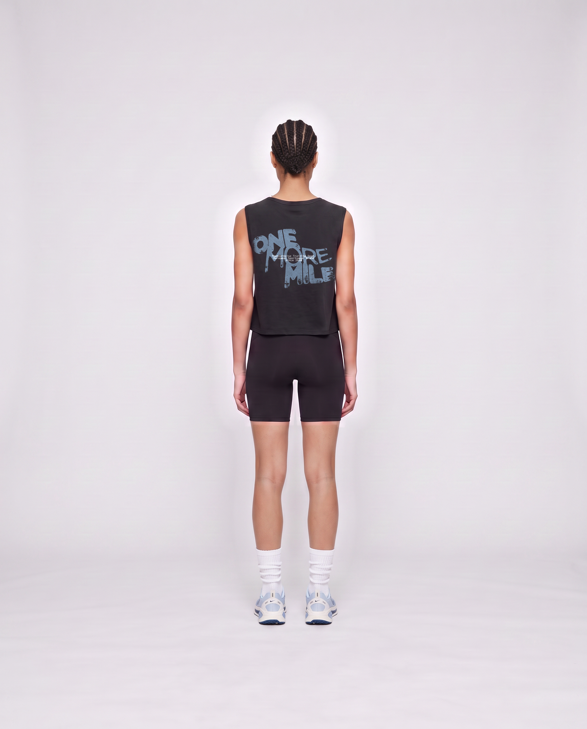 Model wearing the One More Mile cropped tank top in black — back view with the dripping ONE MORE MILE graffiti print in slate blue — View 4

