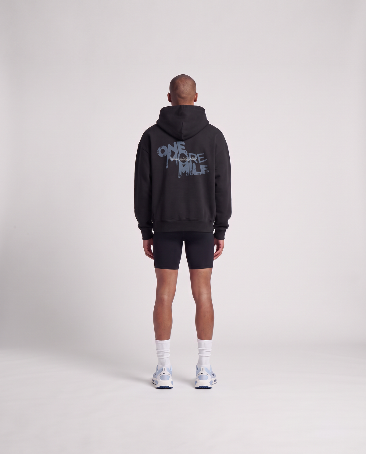 Model wearing the One More Mile oversize hoodie in black — back view with the dripping ONE MORE MILE graffiti print in slate blue