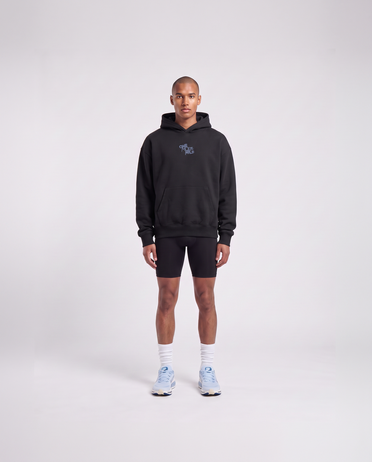 Model wearing the One More Mile oversize hoodie in black — front view with the ONE MORE MILE graffiti mark at the chest in slate blue — View 2

