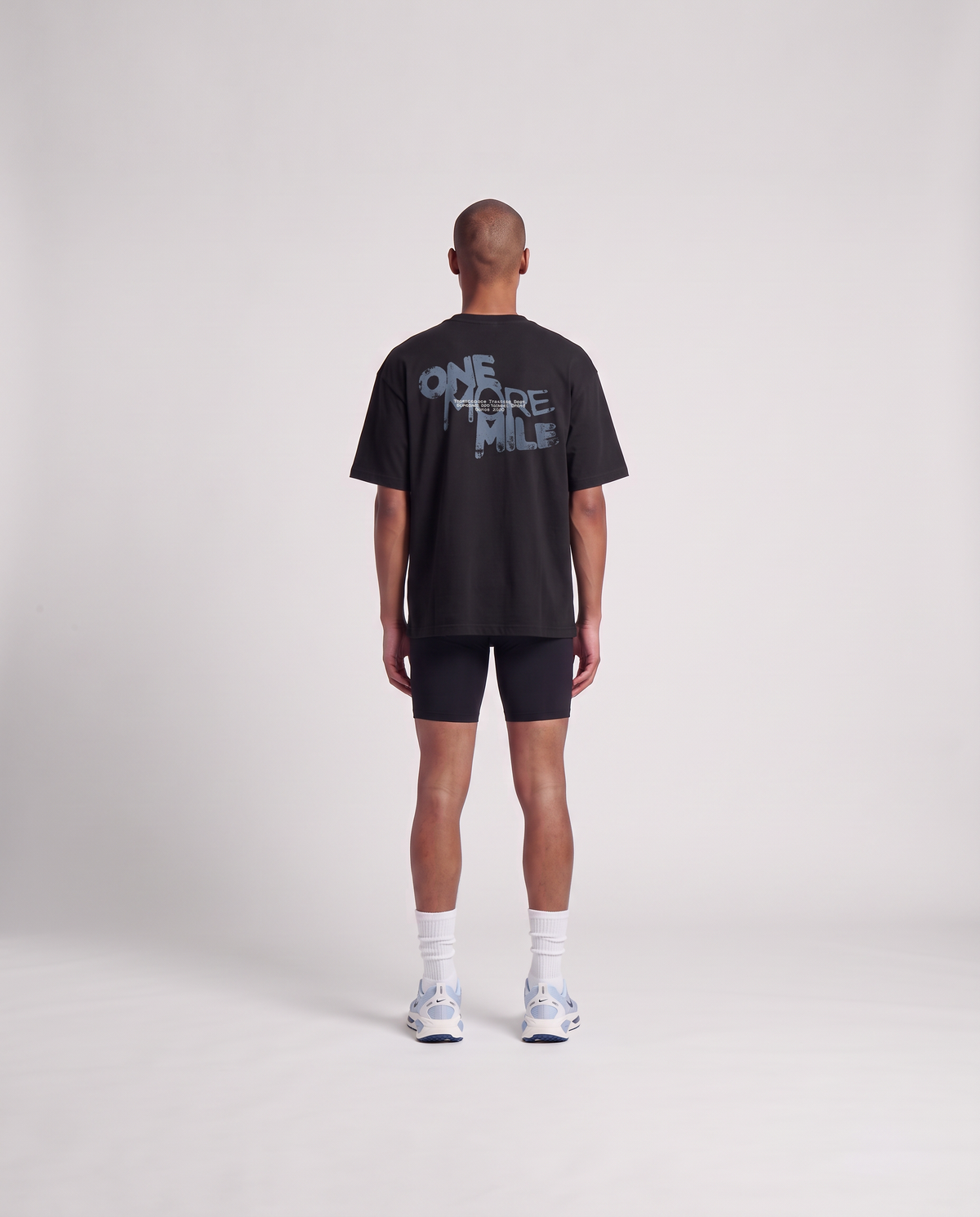 Model wearing the One More Mile oversize t-shirt in black — back view with the dripping ONE MORE MILE graffiti print in slate blue