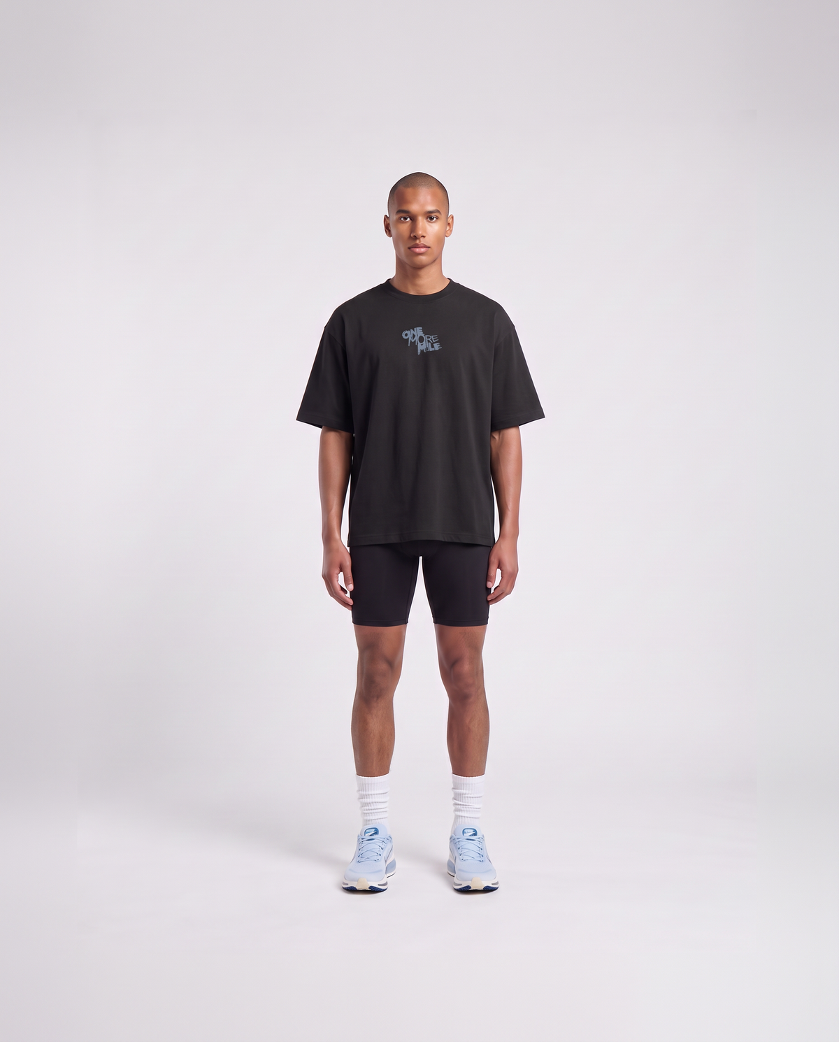 Model wearing the One More Mile oversize t-shirt in black — front view with the ONE MORE MILE graffiti mark at the chest in slate blue — View 2
