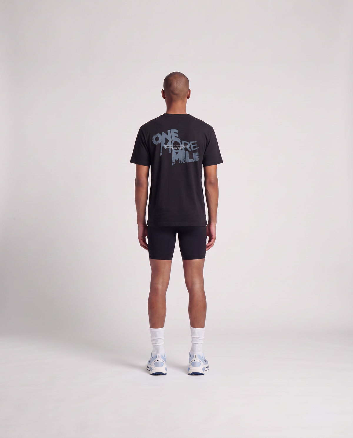 Model wearing the One More Mile t-shirt in black — back view with the dripping ONE MORE MILE graffiti print in slate blue — View 4
