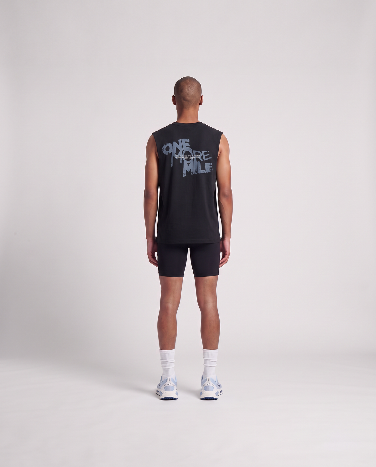 Model wearing the One More Mile tank top in black — back view with the dripping ONE MORE MILE graffiti print in slate blue — View 4
