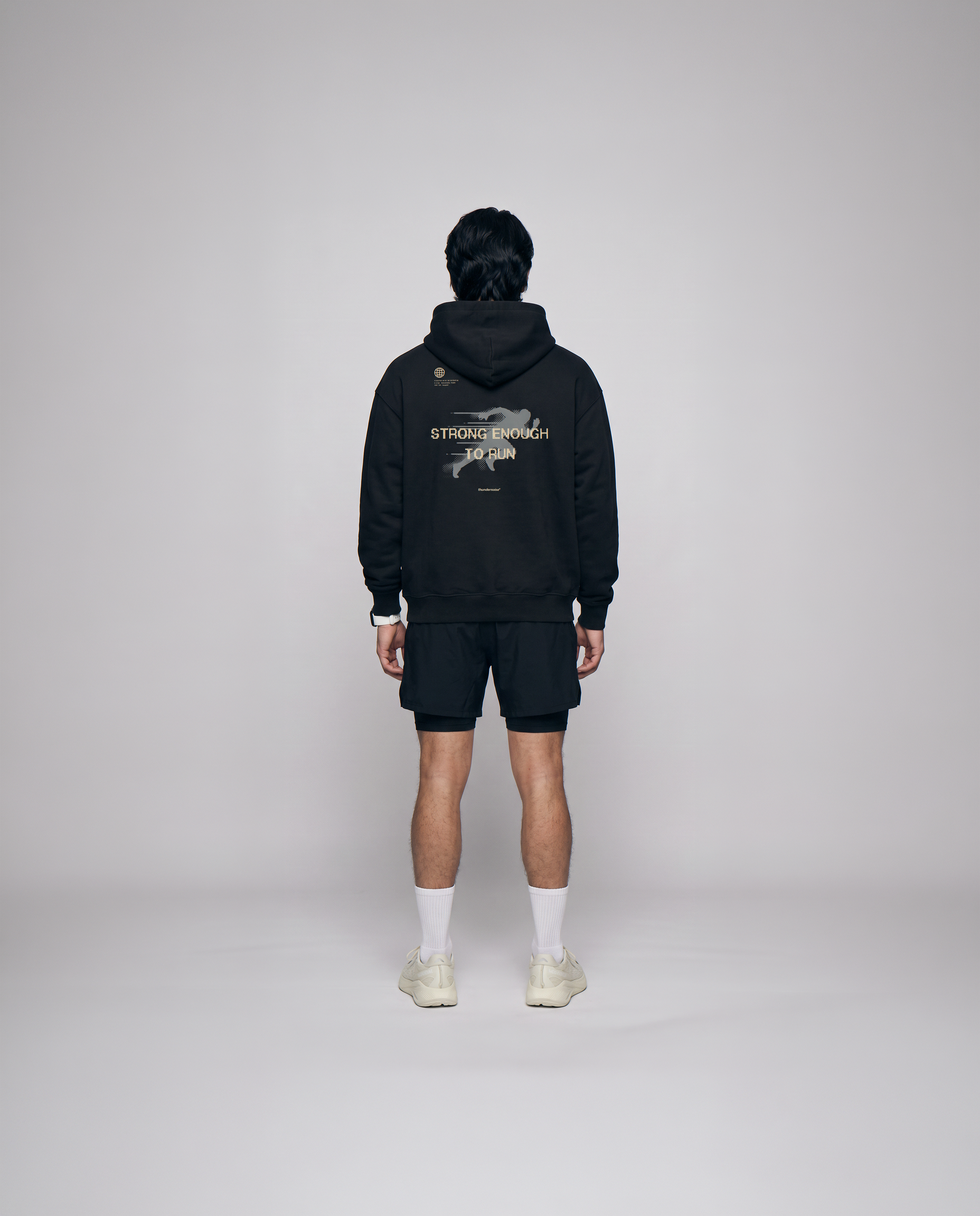 Model wearing the Strong Enough to Run oversize hoodie in black — back view with the STRONG ENOUGH TO RUN halftone runner print