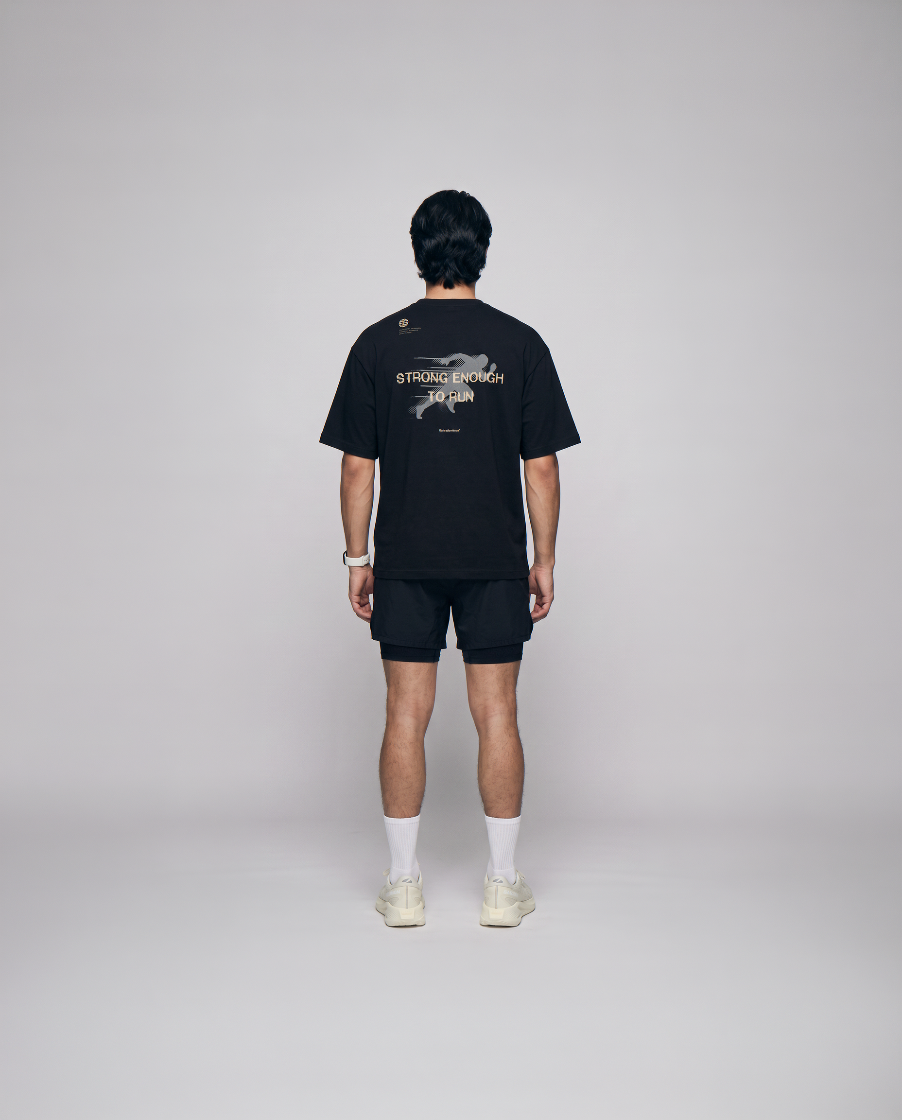 Model wearing the Strong Enough to Run oversize t-shirt in black — back view with the STRONG ENOUGH TO RUN halftone runner print